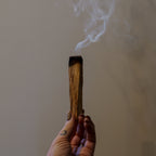 Hand holding a smoking incense stick against a neutral background