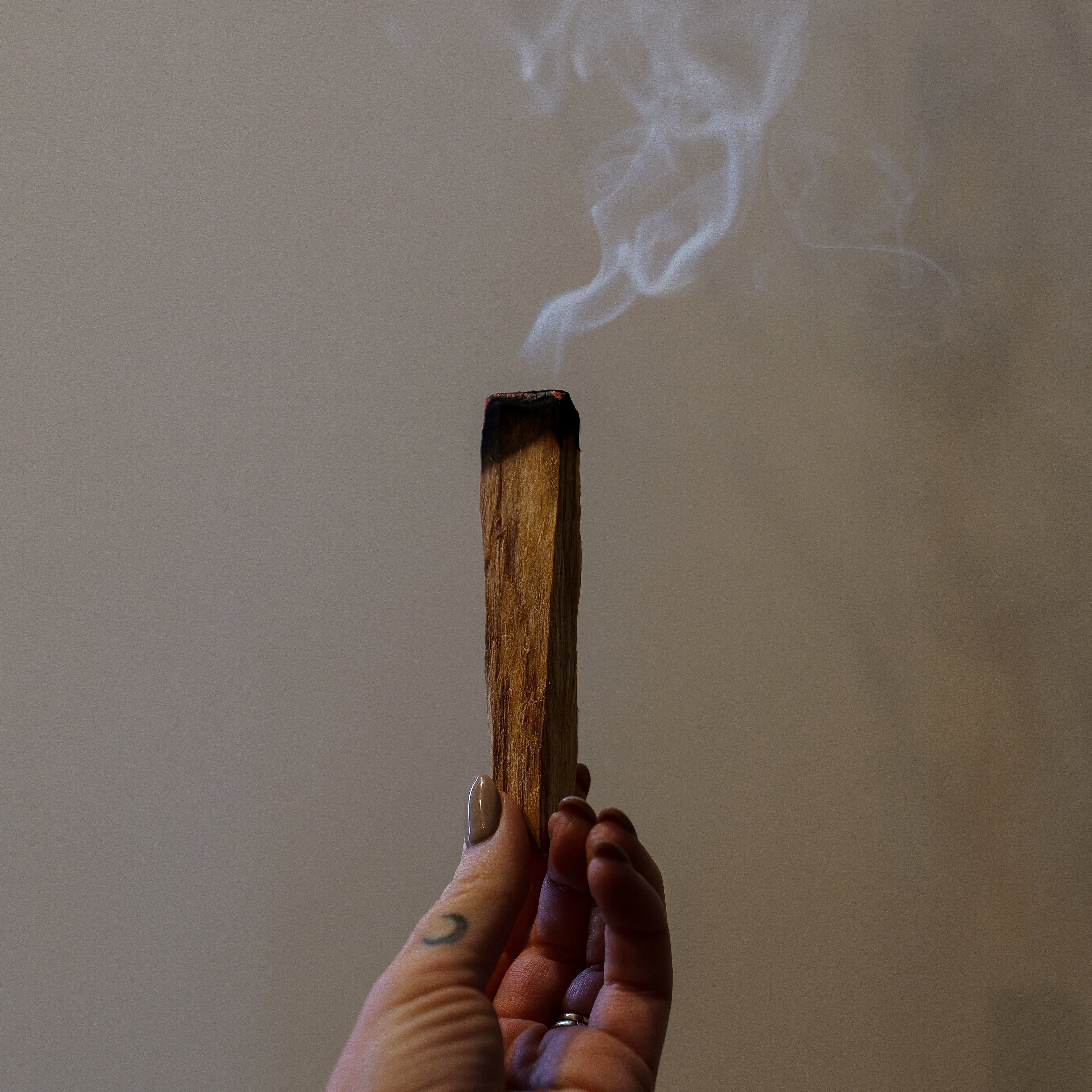 Hand holding a smoking incense stick against a neutral background