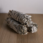 Three bundles of sage on a wooden surface with a plain background