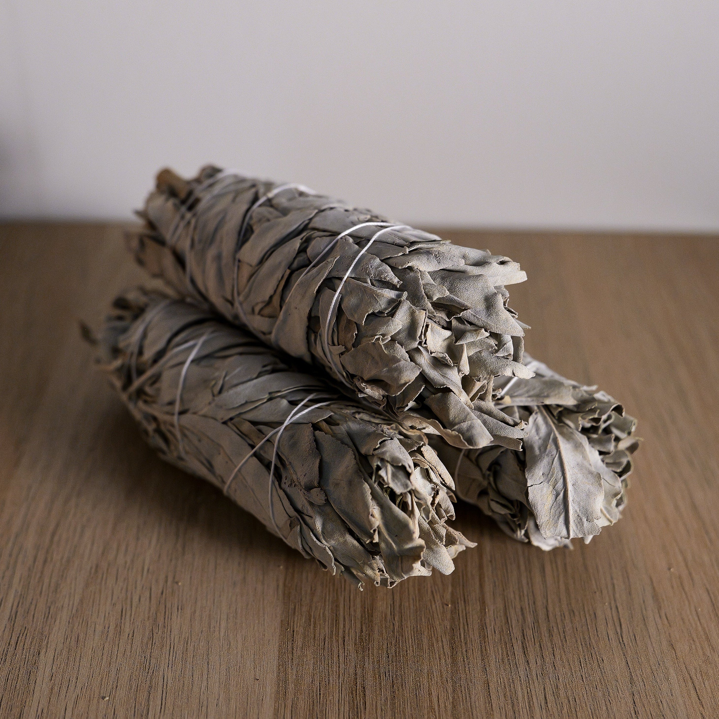 Three bundles of sage on a wooden surface with a plain background
