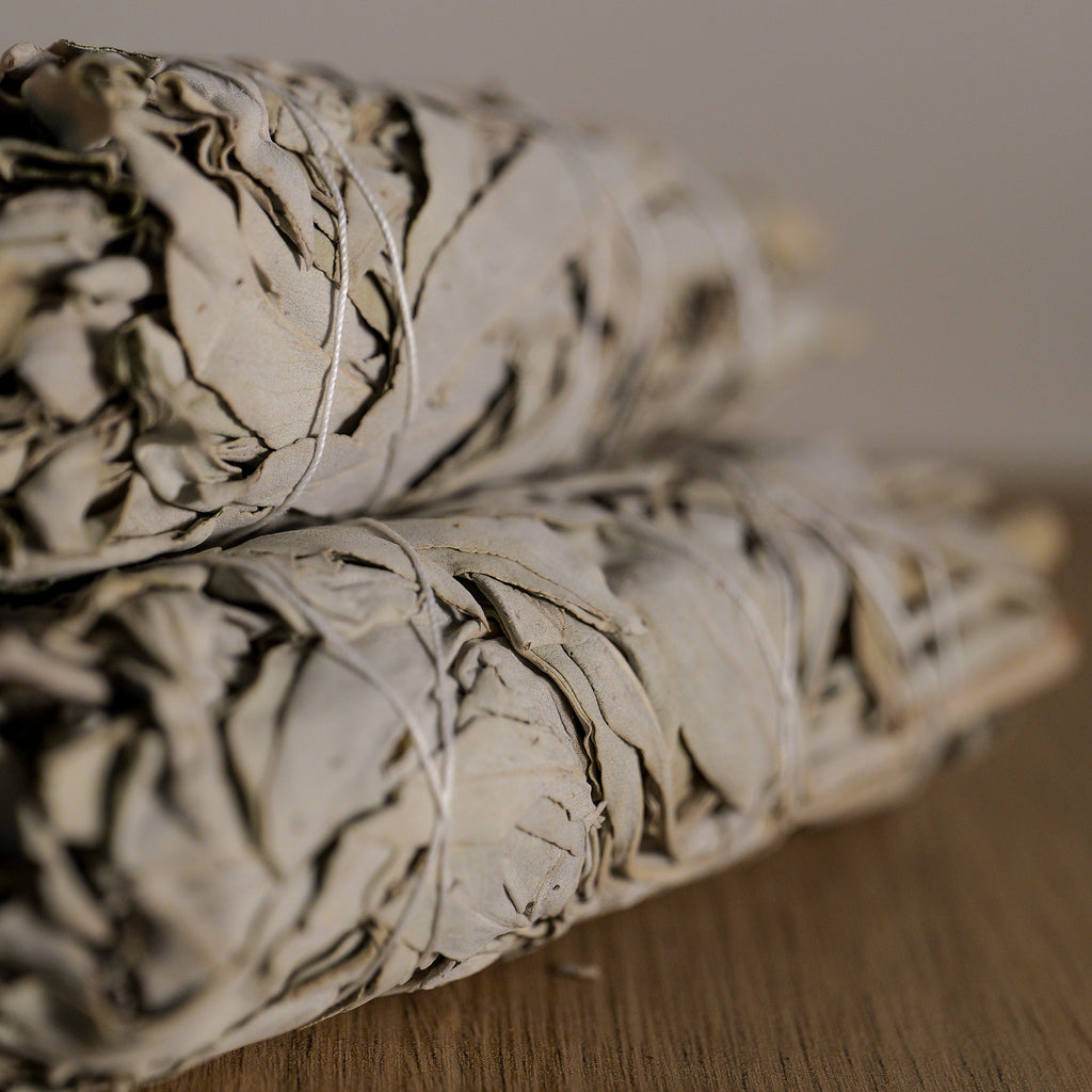 Two bundles of sage on a wooden surface with a neutral background