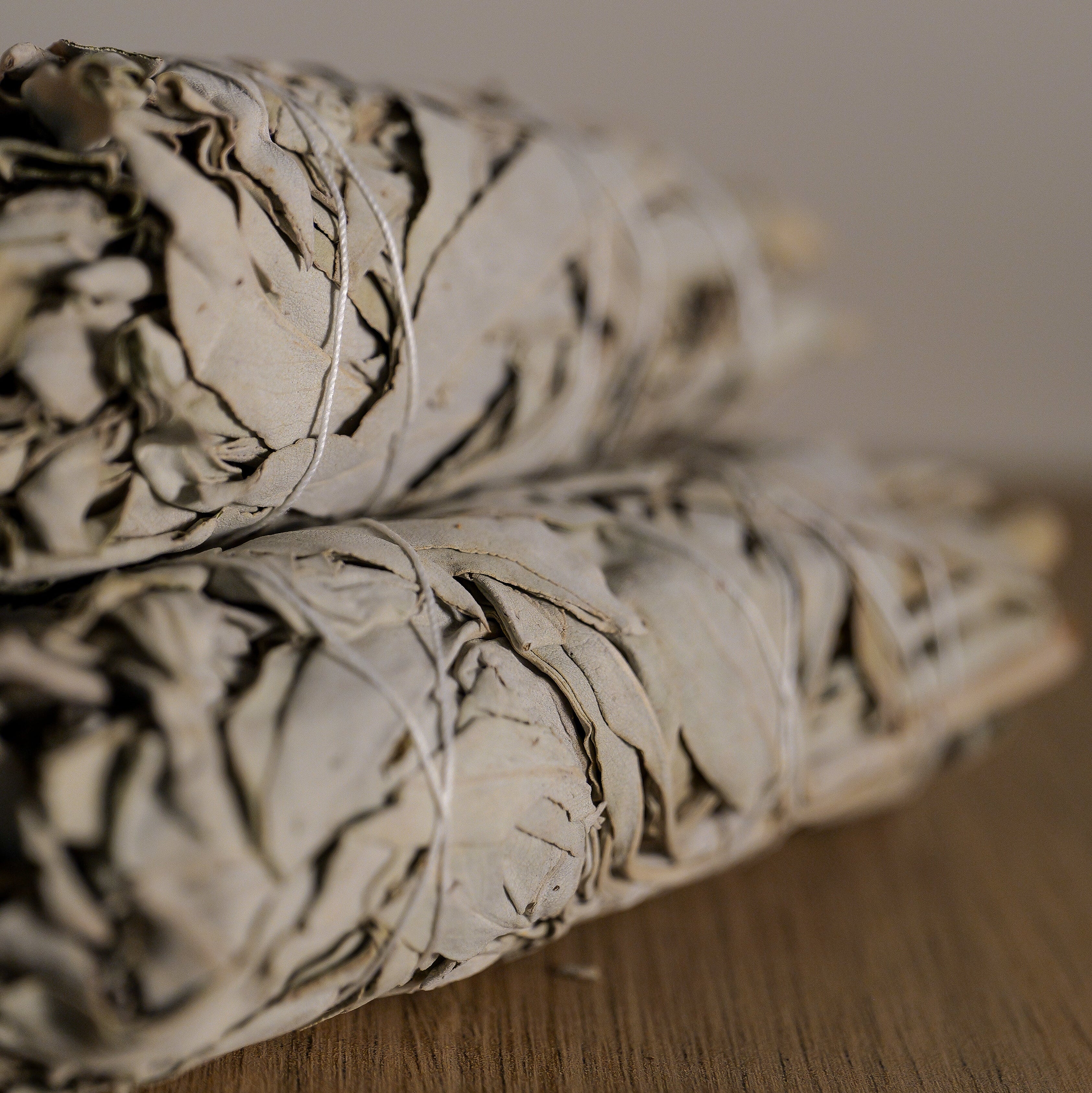 Two bundles of sage on a wooden surface with a neutral background