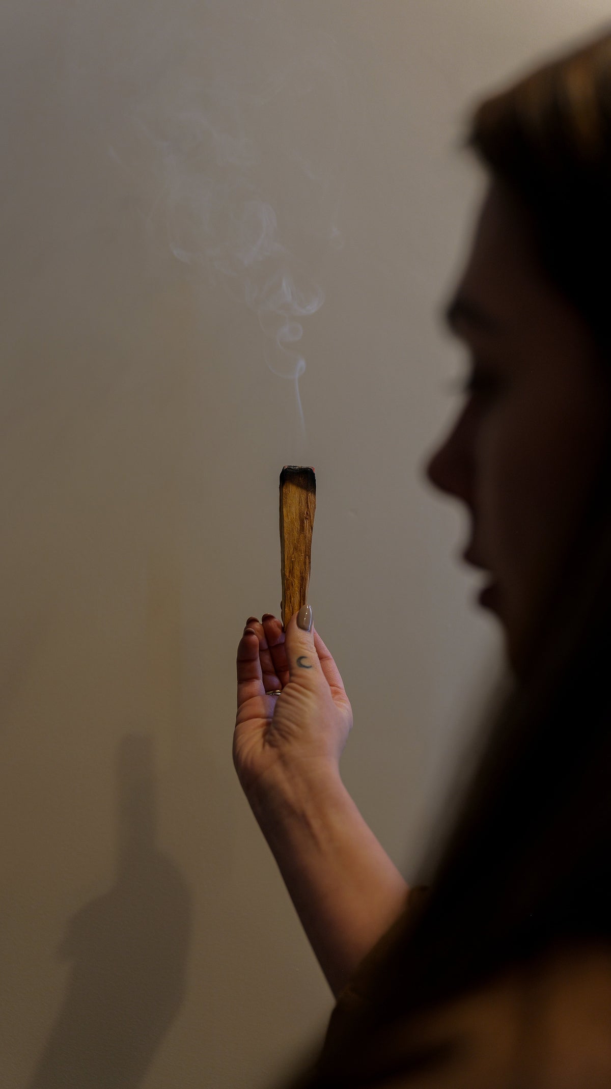 Person holding a lit incense stick against a plain background