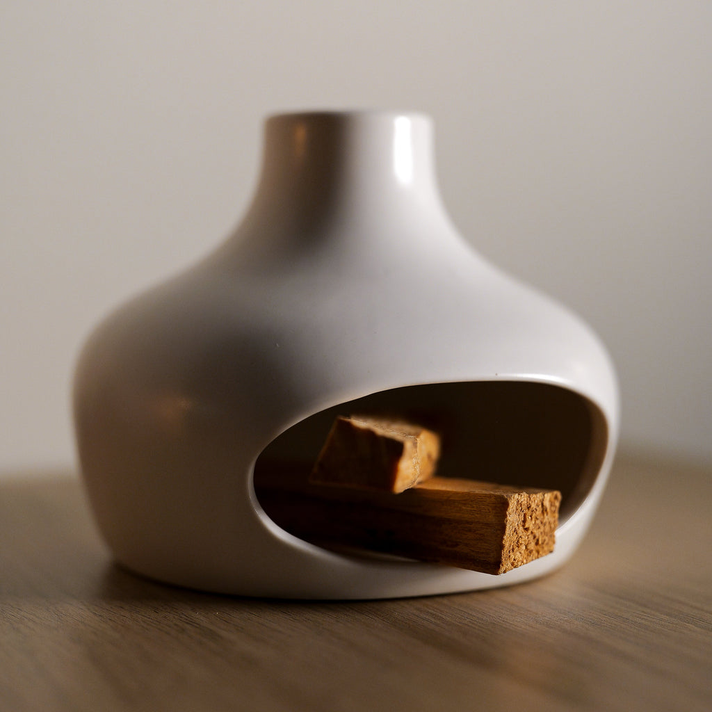 White ceramic vase with a small opening containing Palo Santo on a wooden surface.