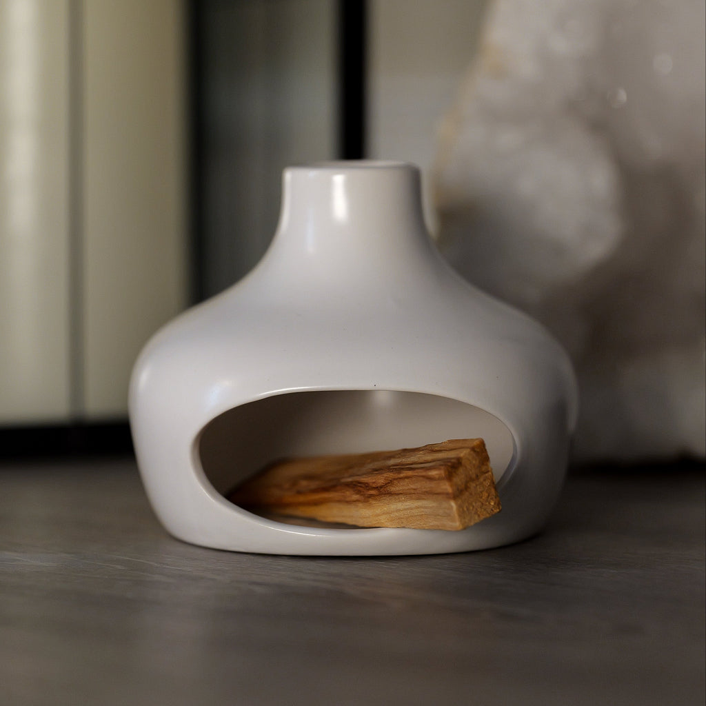 White ceramic holder with a small stack of holy wood on a dark surface