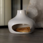 White ceramic holder with a small stack of holy wood on a dark surface