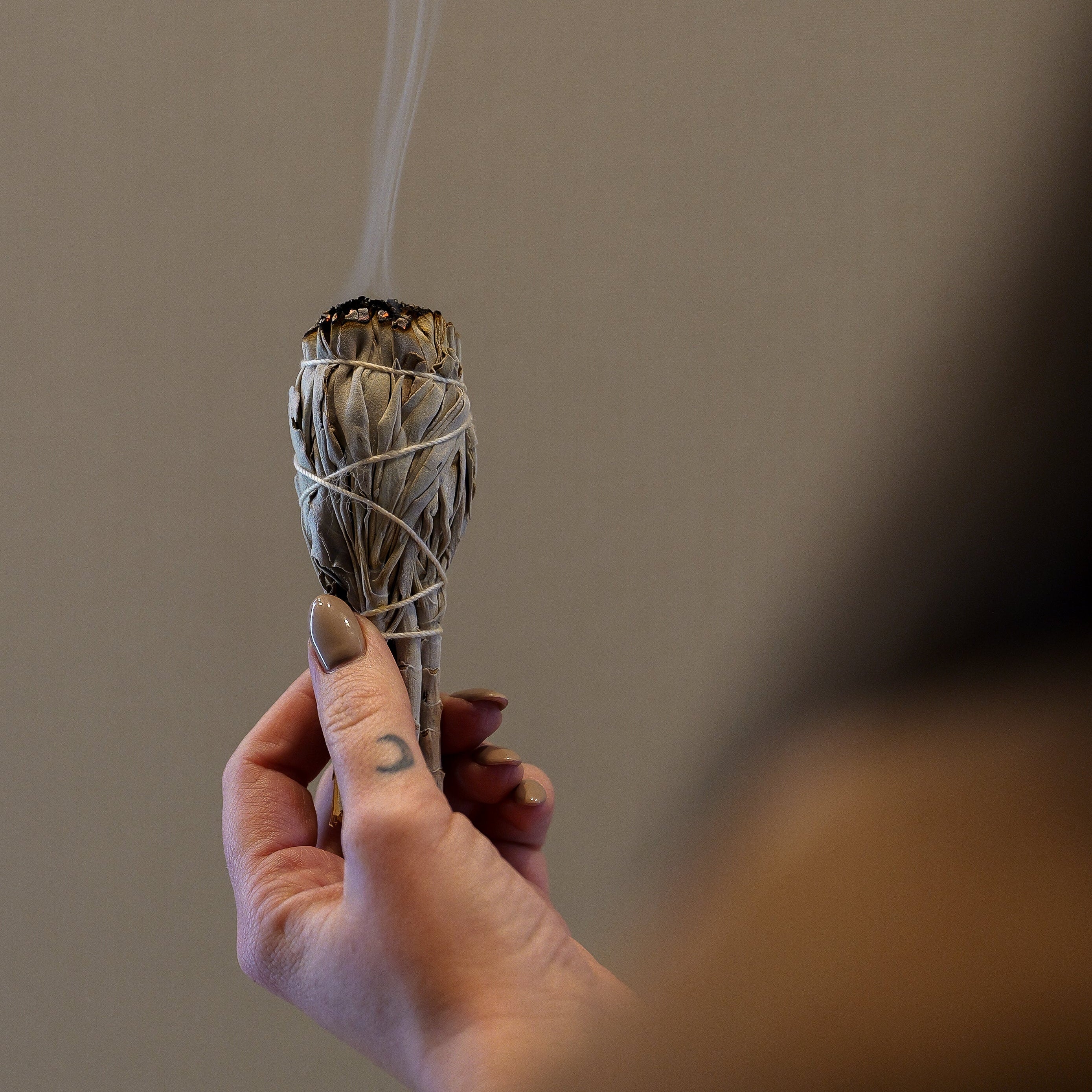 Hand holding a smoldering sage bundle with smoke against a neutral background