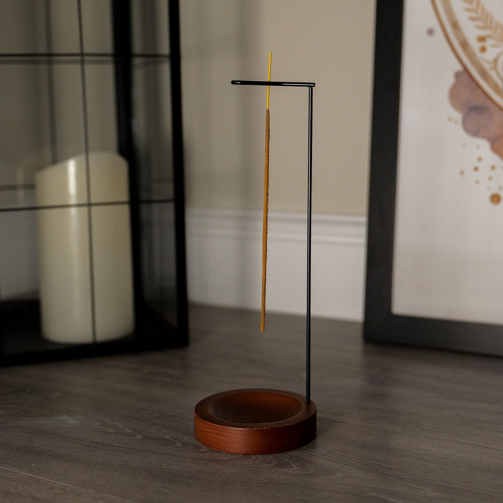 Incense stick holder with a single incense stick on a wooden floor.
