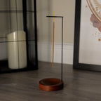 Incense stick holder with a single incense stick on a wooden floor.