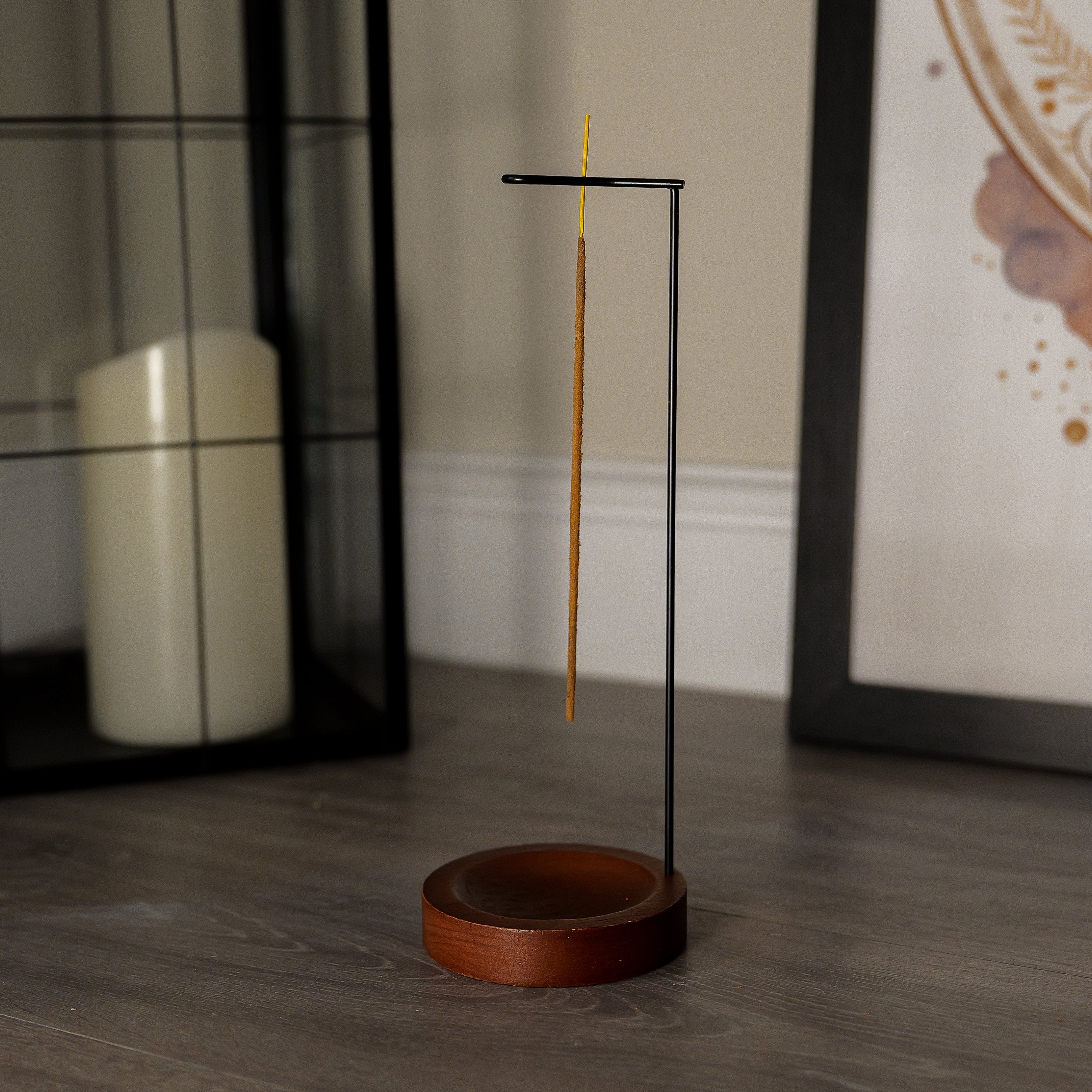 Incense stick holder with a single incense stick on a wooden floor.
